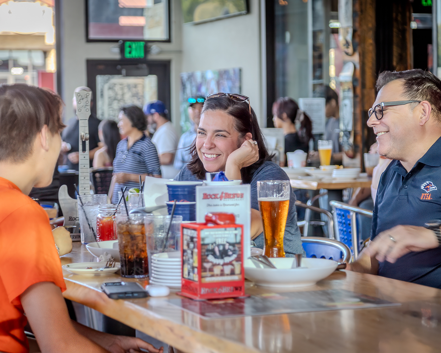 A mother and father with their student talking and laughing at a table in a resturant.